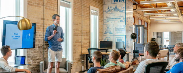 Homme donnant une présentation devant un groupe de personnes assises dans un espace de coworking moderne.