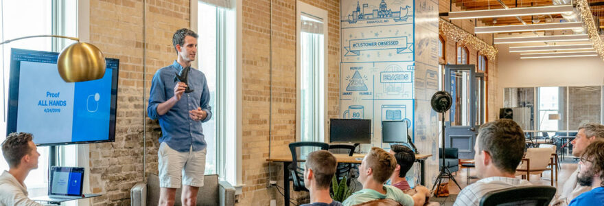 Homme donnant une présentation devant un groupe de personnes assises dans un espace de coworking moderne.